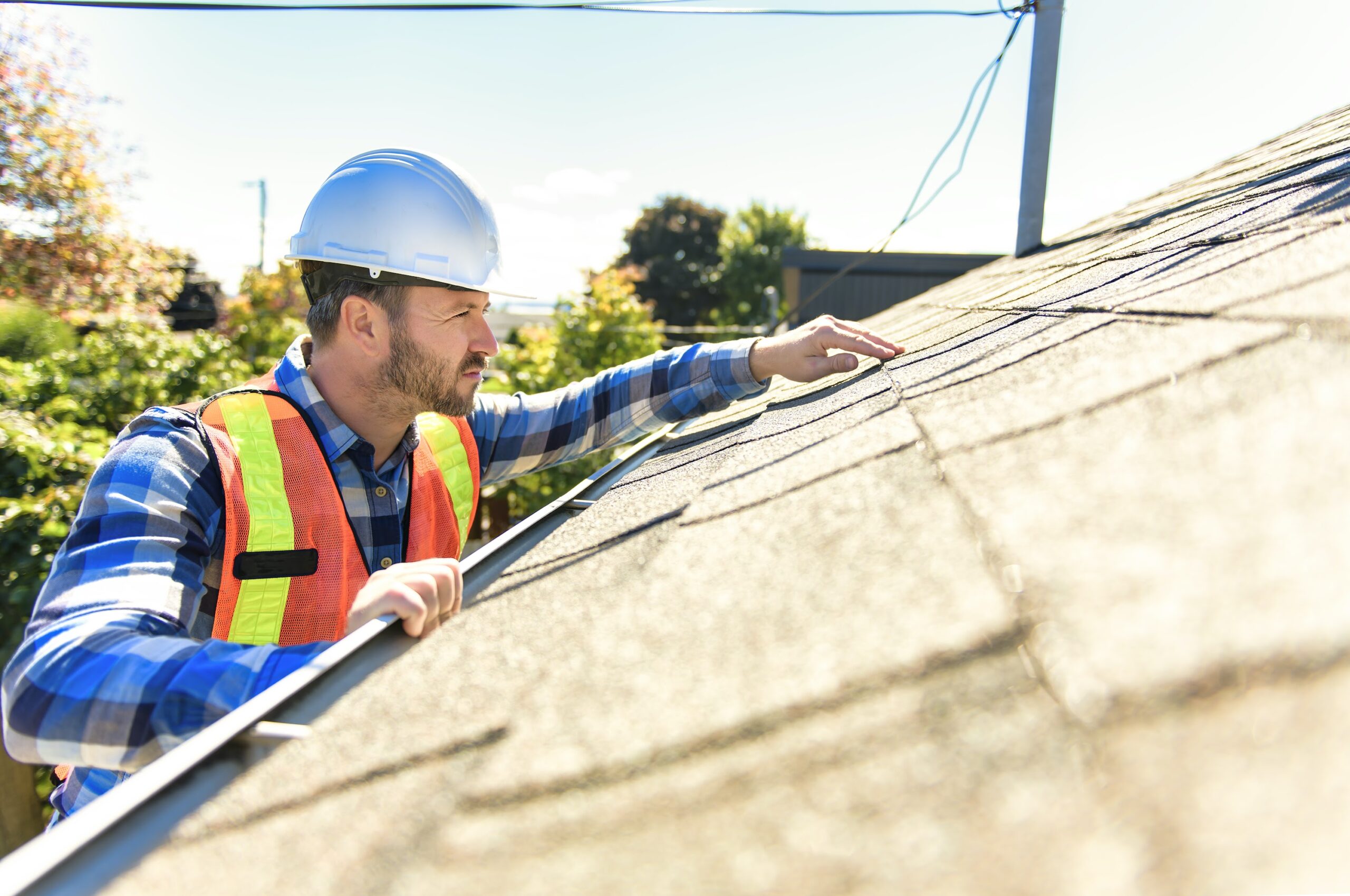 A man with hard hat standing on steps inspecting house roof